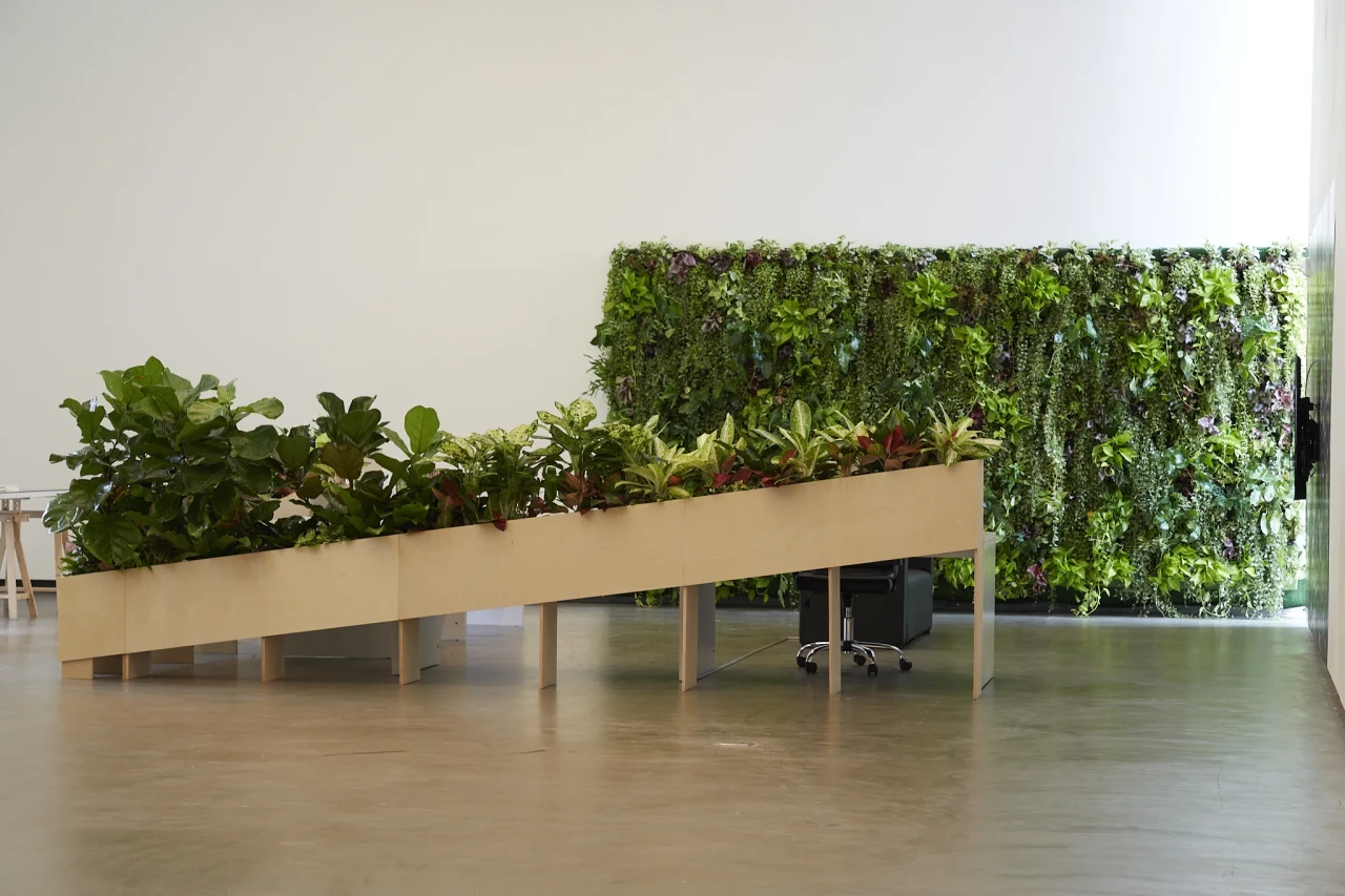Ho rui an, A Petropolis in a Garden with A Long View, 2024. Video installation with laser etched crystal, acrylic awards, books, globe-shaped bookends, office table and chair, wall shelves, planter boxes, assorted plants and wallpaper. , Dimension variable.. Photo: Thakueng Withusuwan. Courtesy of the Jim Thompson Art Center and the James H.W. Thompson Foundation © Jim Thompson Art Center